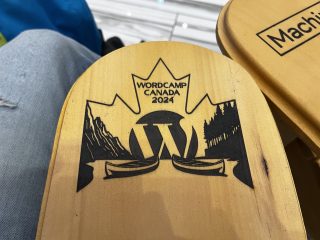 WordCamp Canada logo on arm of Muskoka chair - it shows two canoes on a lake in the mountains, with a backdrop of a maple leaf and the WordPress logo